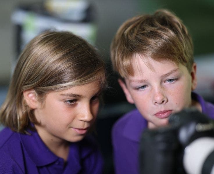Two boys looking in a large camera they are holding