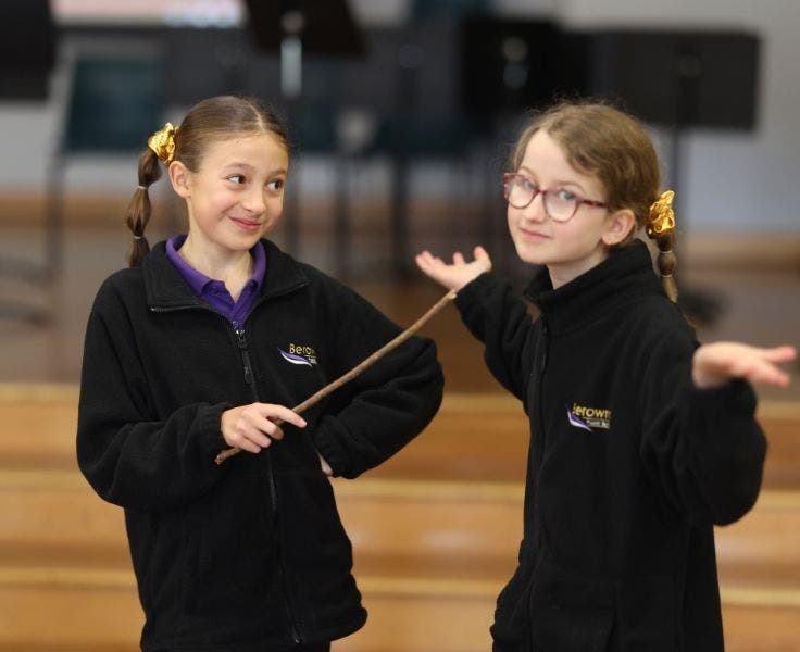 Two girls, one has a wand and the other has her hands out, they are in a drama class